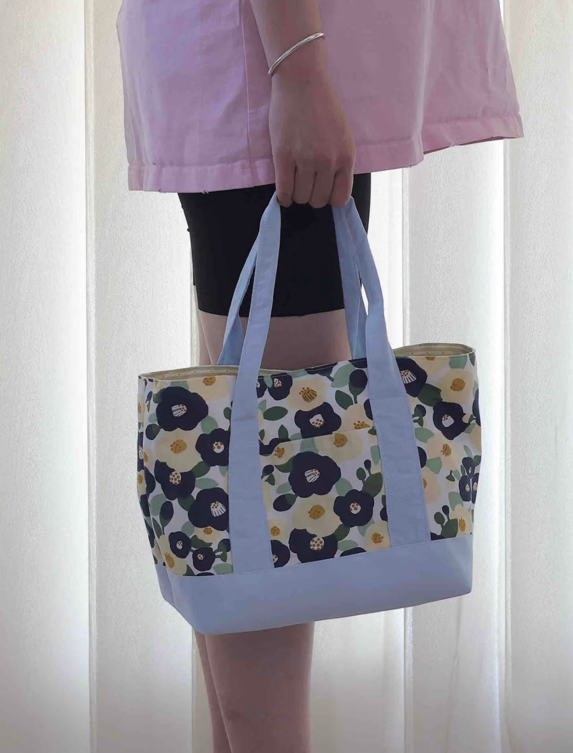 Person holding a floral-patterned tote bag against a white curtain background