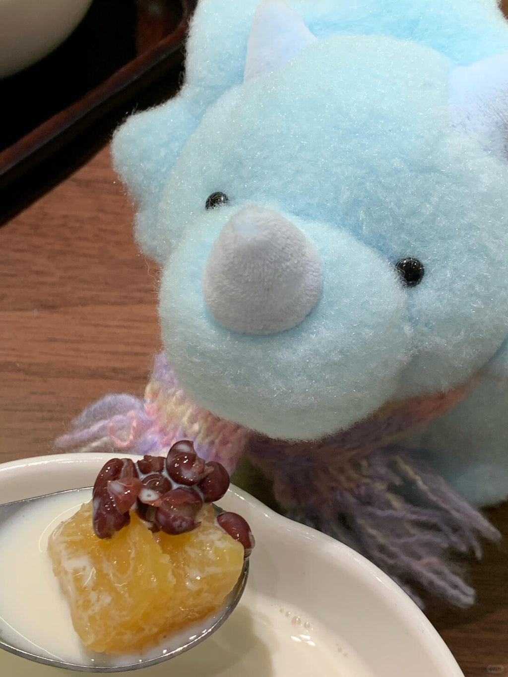 Spoon with dessert and red berries in front of a blue dinosaur plush toy on a wooden surface