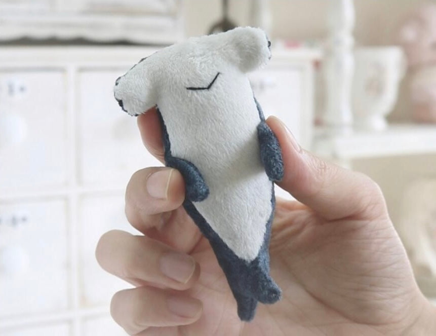 Small plush shark toy held in a hand with a blurred indoor background