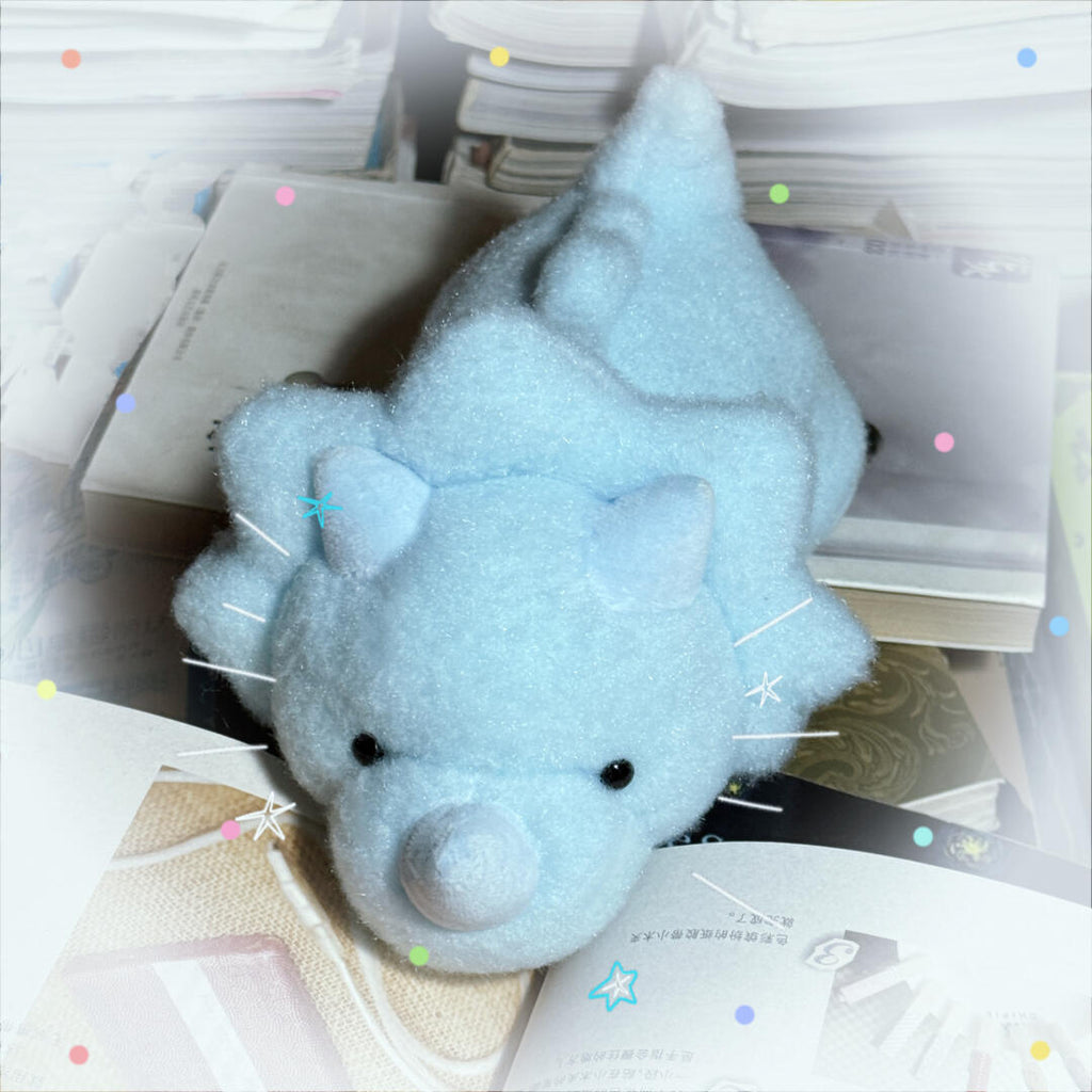 Blue plush toy dinosaur on a stack of books with decorative elements.
