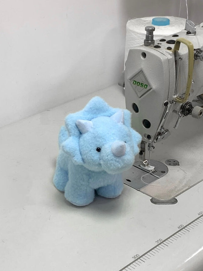 Blue plush dinosaur toy next to a sewing machine on a white surface.