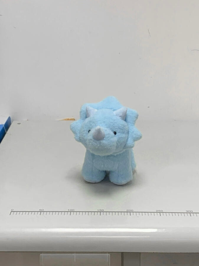 Small blue dinosaur plush toy on a white surface with a ruler for scale.