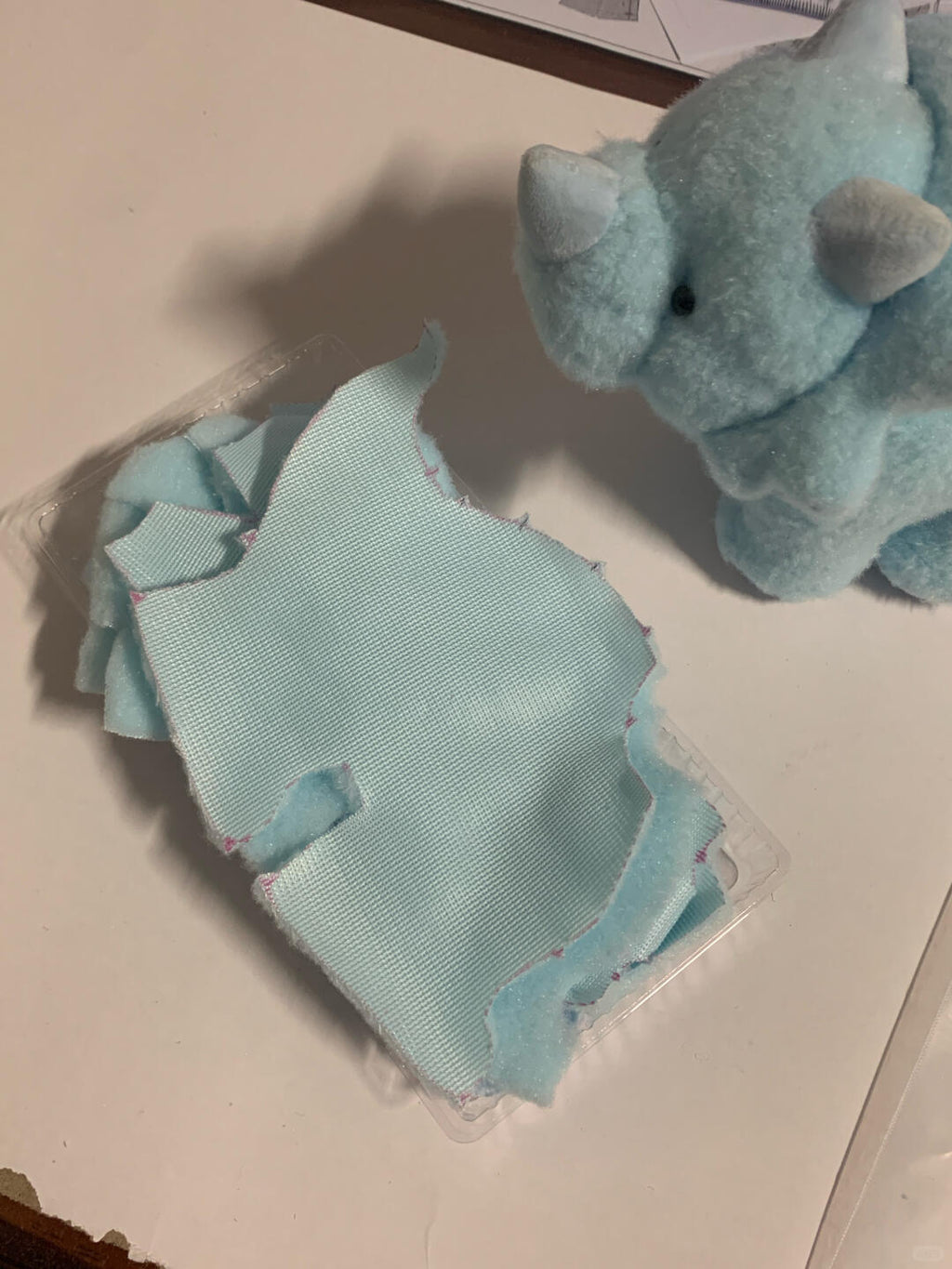 Light blue dinosaur fabric swatches on a clear plastic sheet with a toy dinosaur in the background.