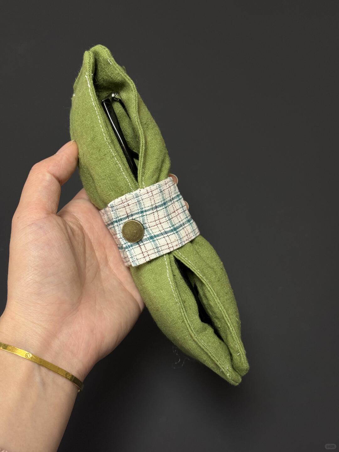 Green fabric object with a plaid band held by a hand against a dark background