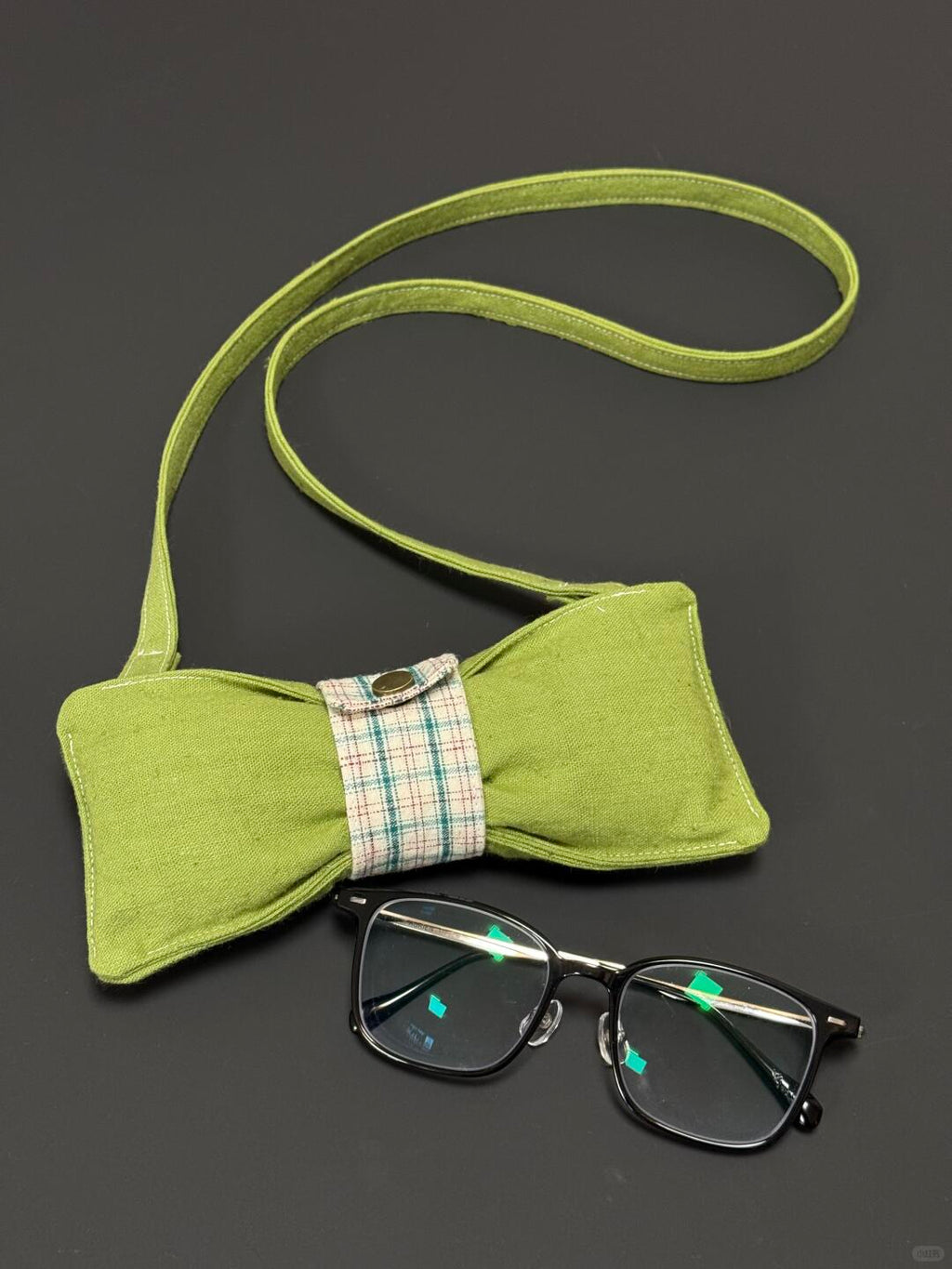 Green bow tie with a plaid ribbon and glasses on a dark background