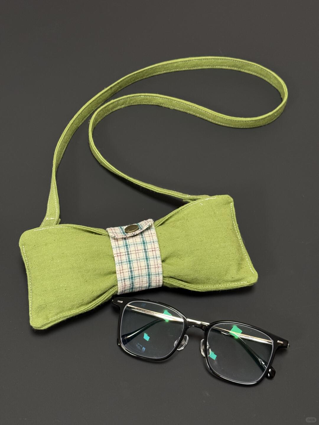 Green bow tie with a plaid ribbon and glasses on a dark background