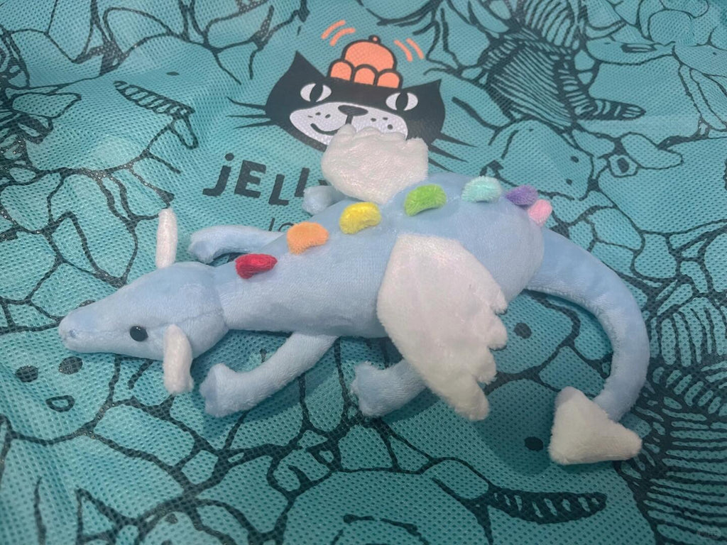 Finished blue Sky Dragon plush sewing pattern sample lying on its side with white wings and rainbow spines