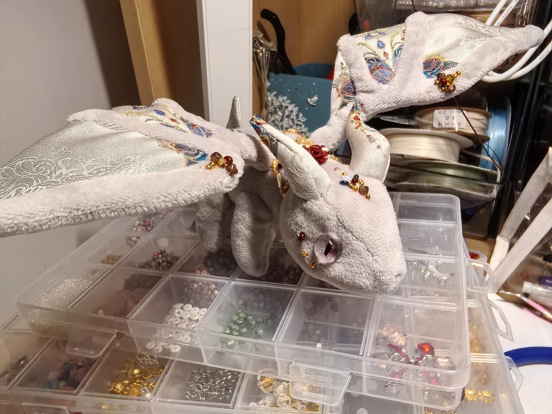 Gray stuffed animal with decorative elements on a table with jewelry boxes.