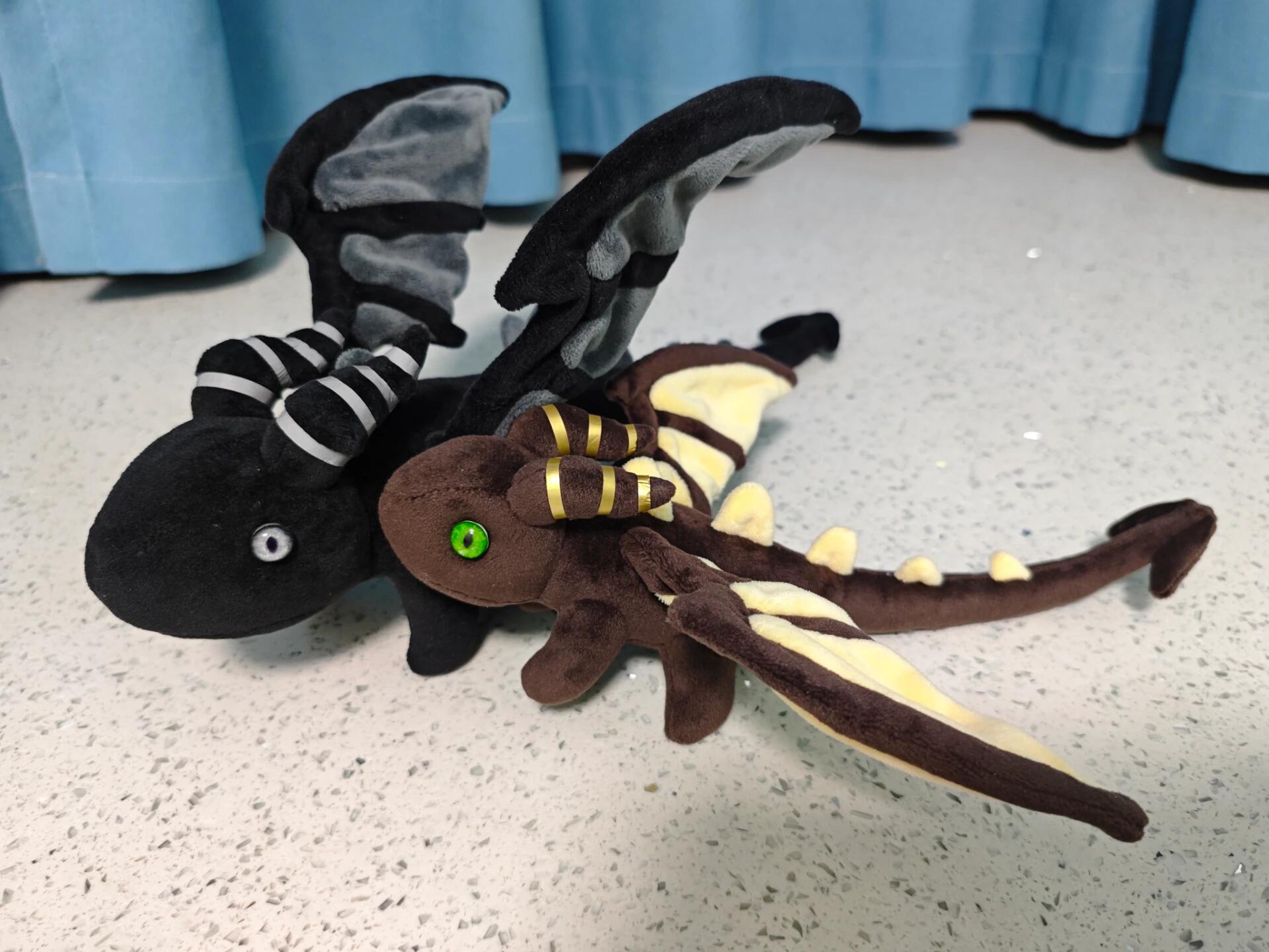 Plush dragon toy with black, brown, and white colors on a light gray surface.