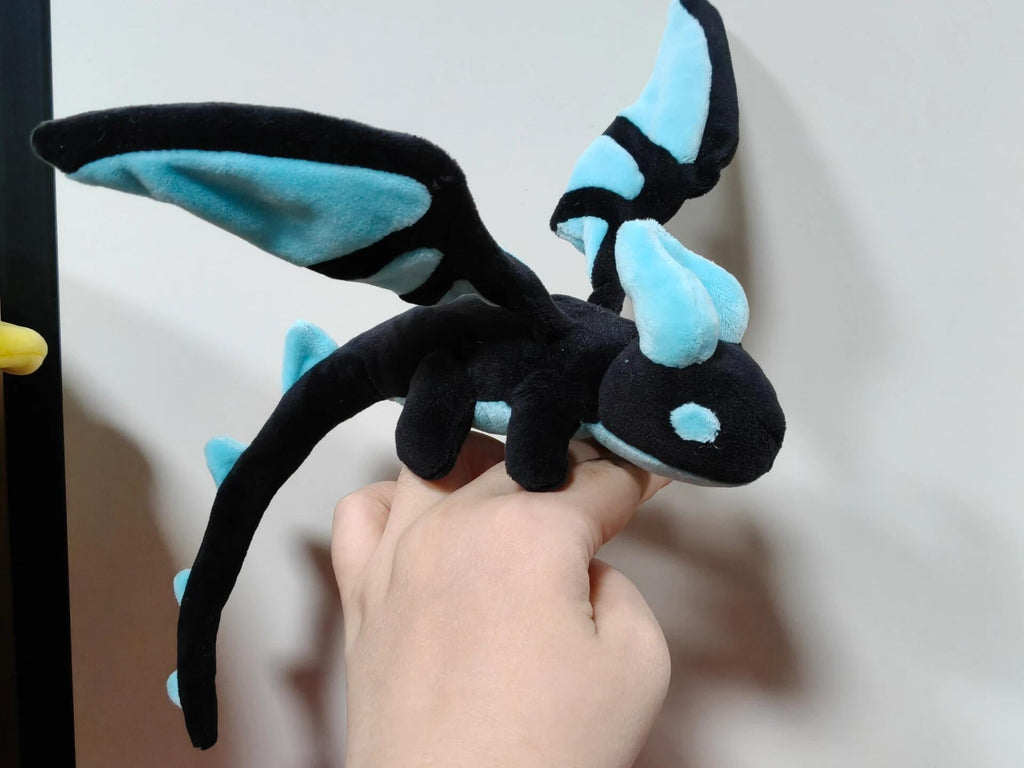 Plush dragon toy with black and blue colors held by a hand against a neutral background