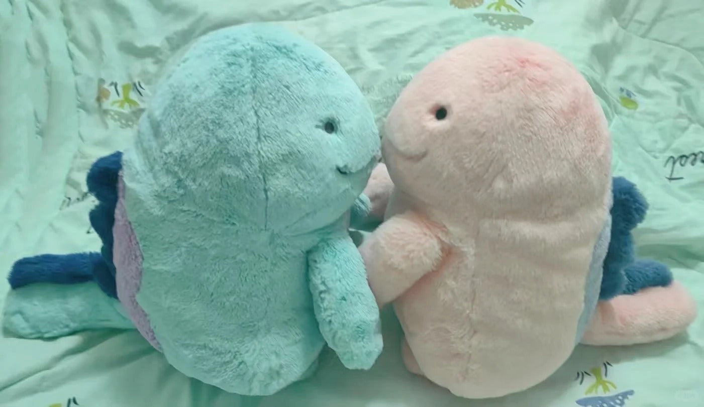 Two plush pokemon Quagsire toys, one light blue with purple side accents and one pale pink, posed together on a light green patterned fabric background.