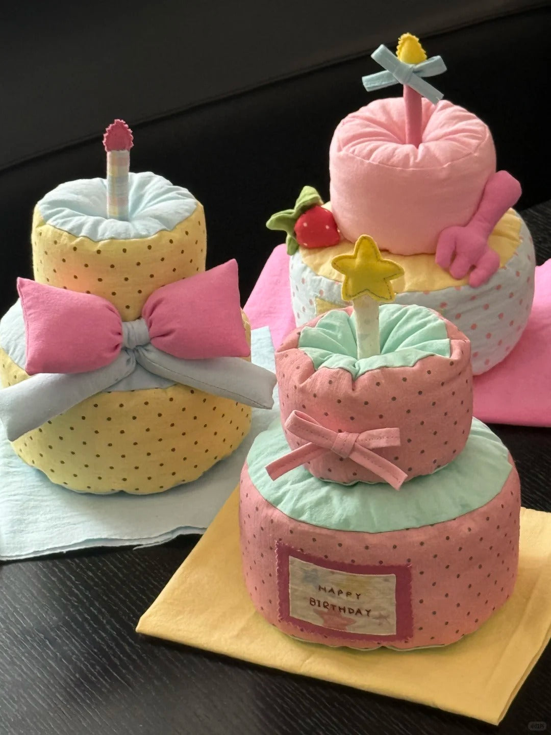 Three soft fabric baby shower games styled like tiered birthday cakes, arranged on napkins on a dark wooden table.