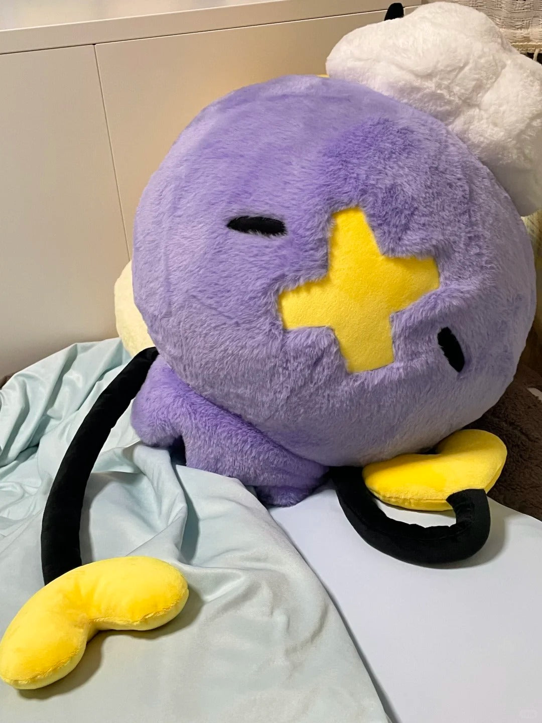 Close-up of an oversized purple Drifloon plush with yellow crossed face patch