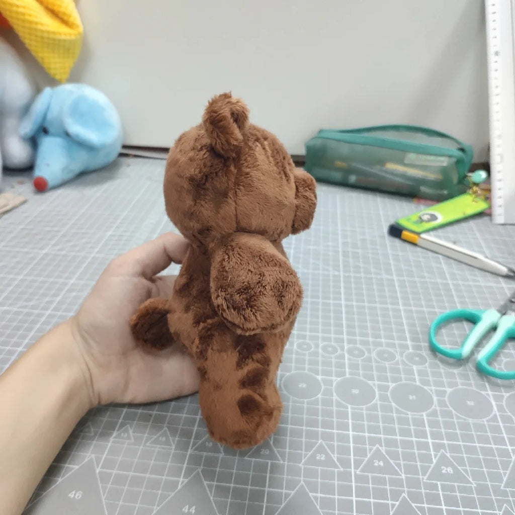 Brown teddy bear held by a hand on a cutting mat with tools in the background