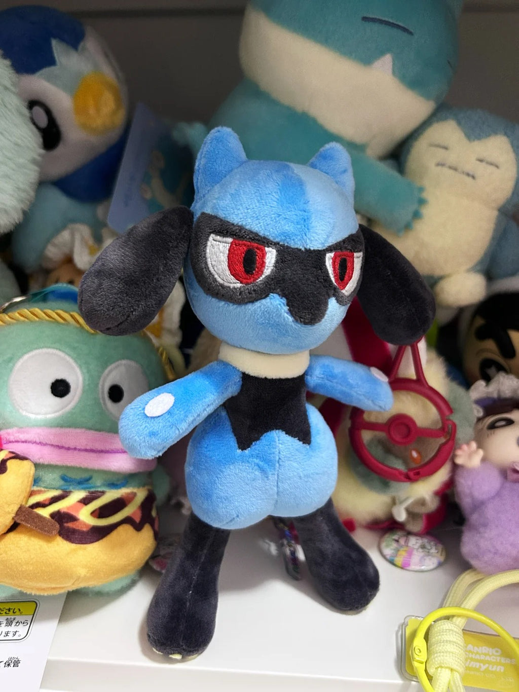 Finished blue Lucario-inspired plush displayed upright among a collection of handmade plush toys