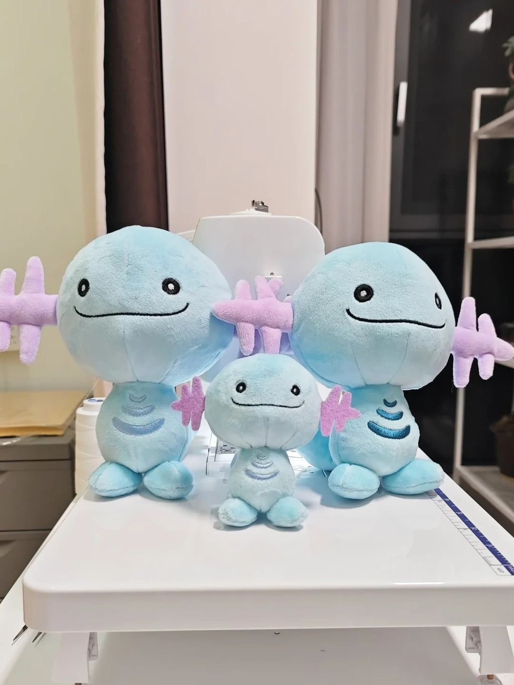 Three Wooper light blue plush toy characters with pink starfish accessories, arranged on a white table in an indoor room setting.