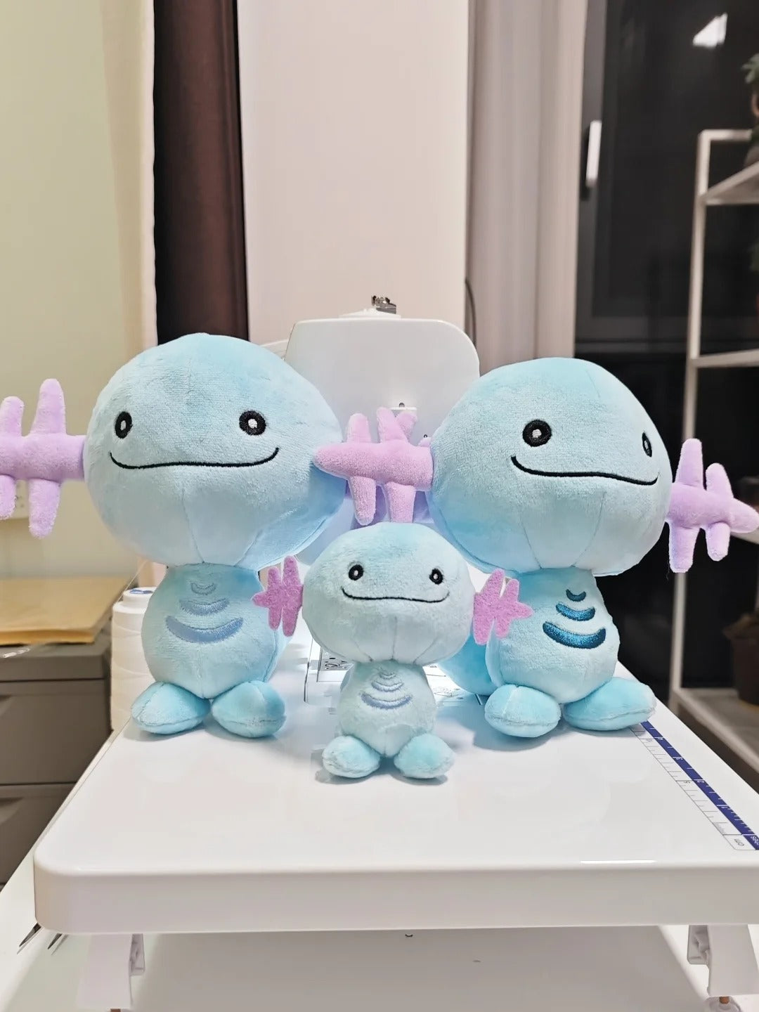 Three Wooper light blue plush toy characters with pink starfish accessories, arranged on a white table in an indoor room setting.
