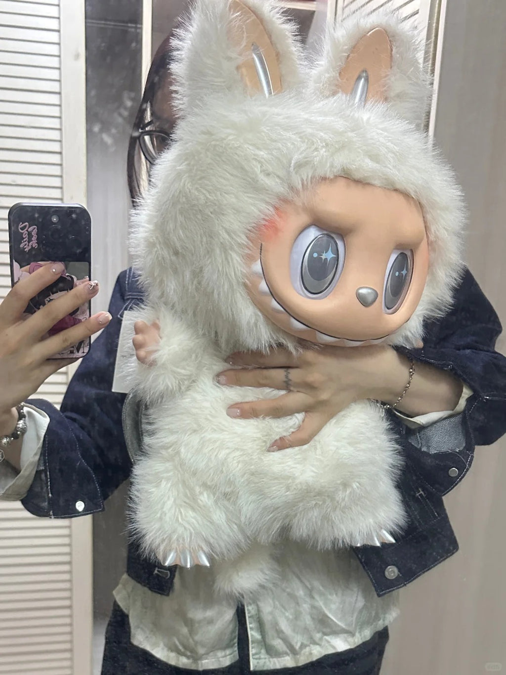 Person holding a fluffy white Zimomo plush toy with large eyes and Labubu ears. 