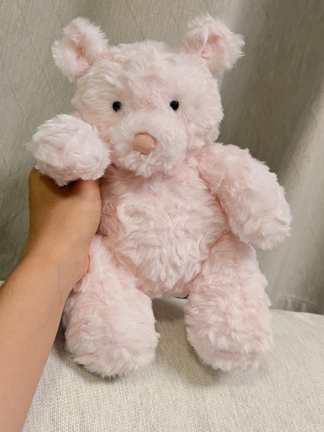Pink teddy bear held by a hand against a neutral background