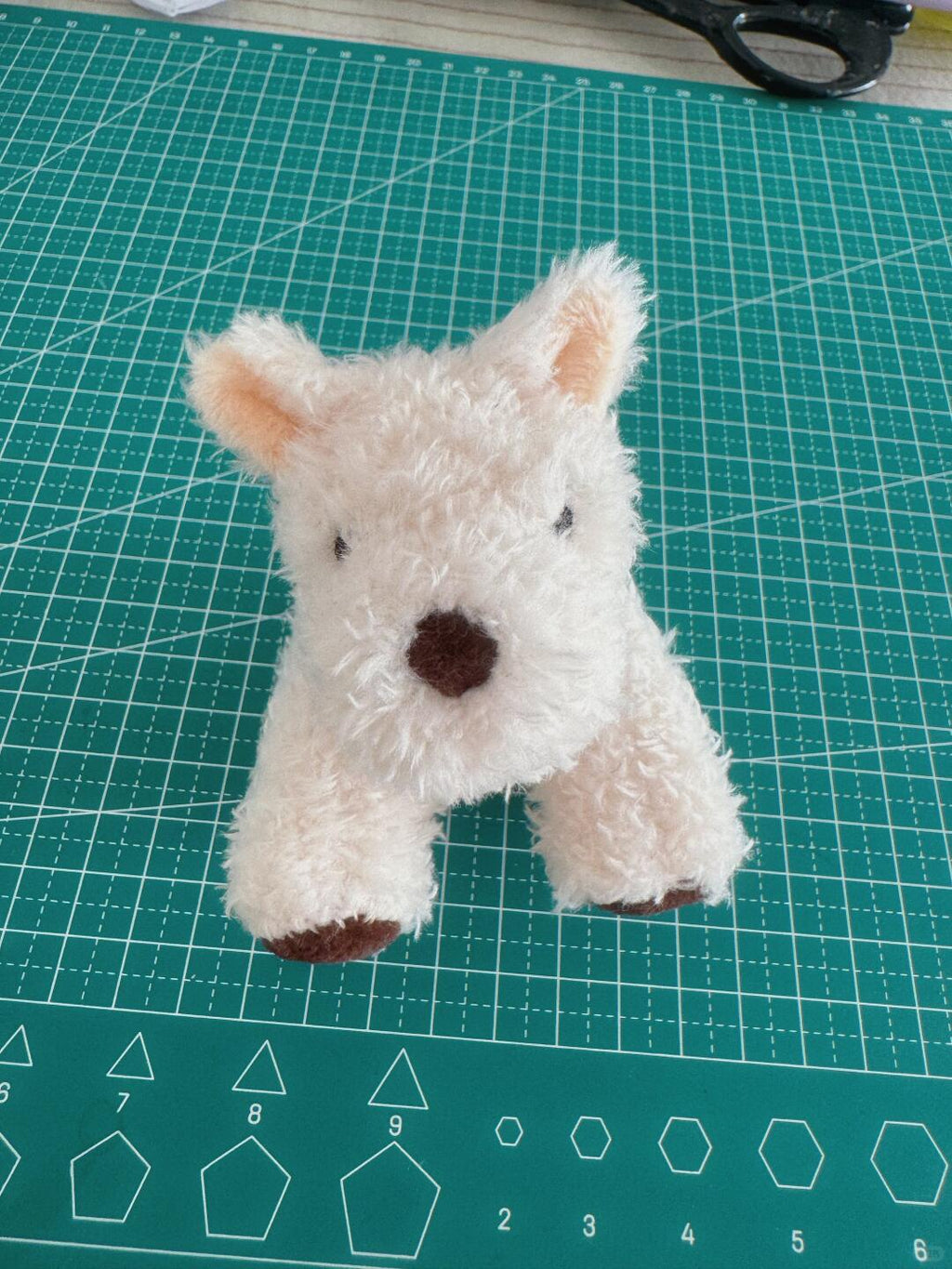 Small white stuffed animal on a green cutting mat with grid lines