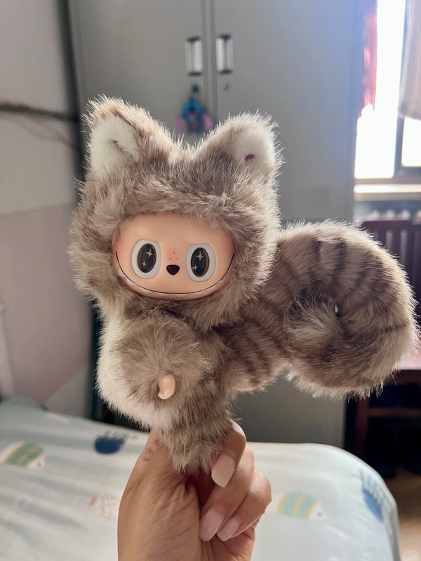 Plush toy resembling a cat with a cartoon face held by a hand in an indoor setting.