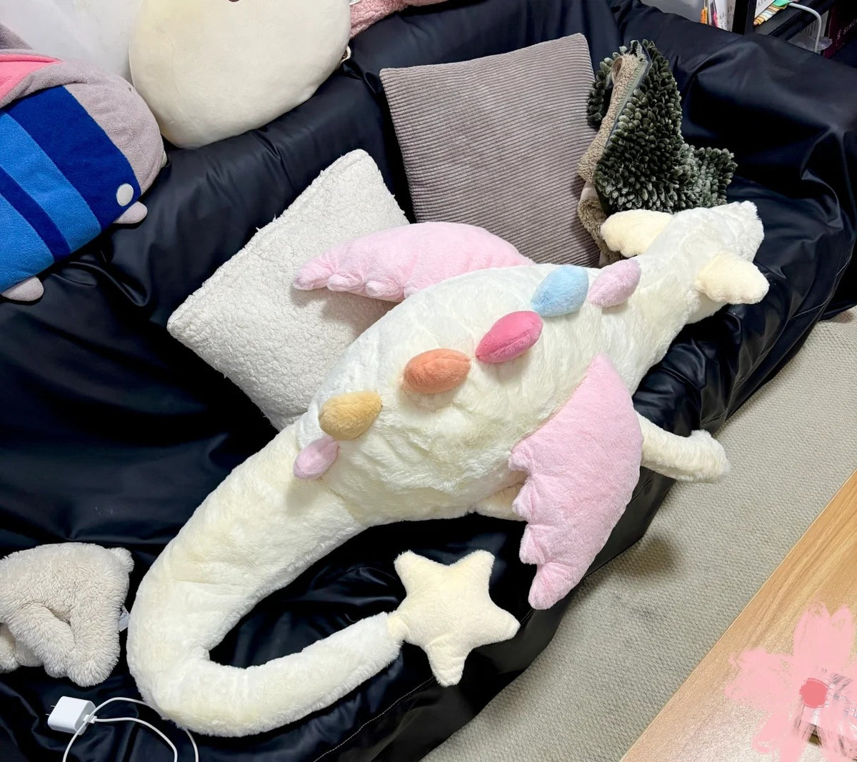 Large cream Sky Dragon plush sewing pattern sample with pink wings and pastel rainbow spines on sofa