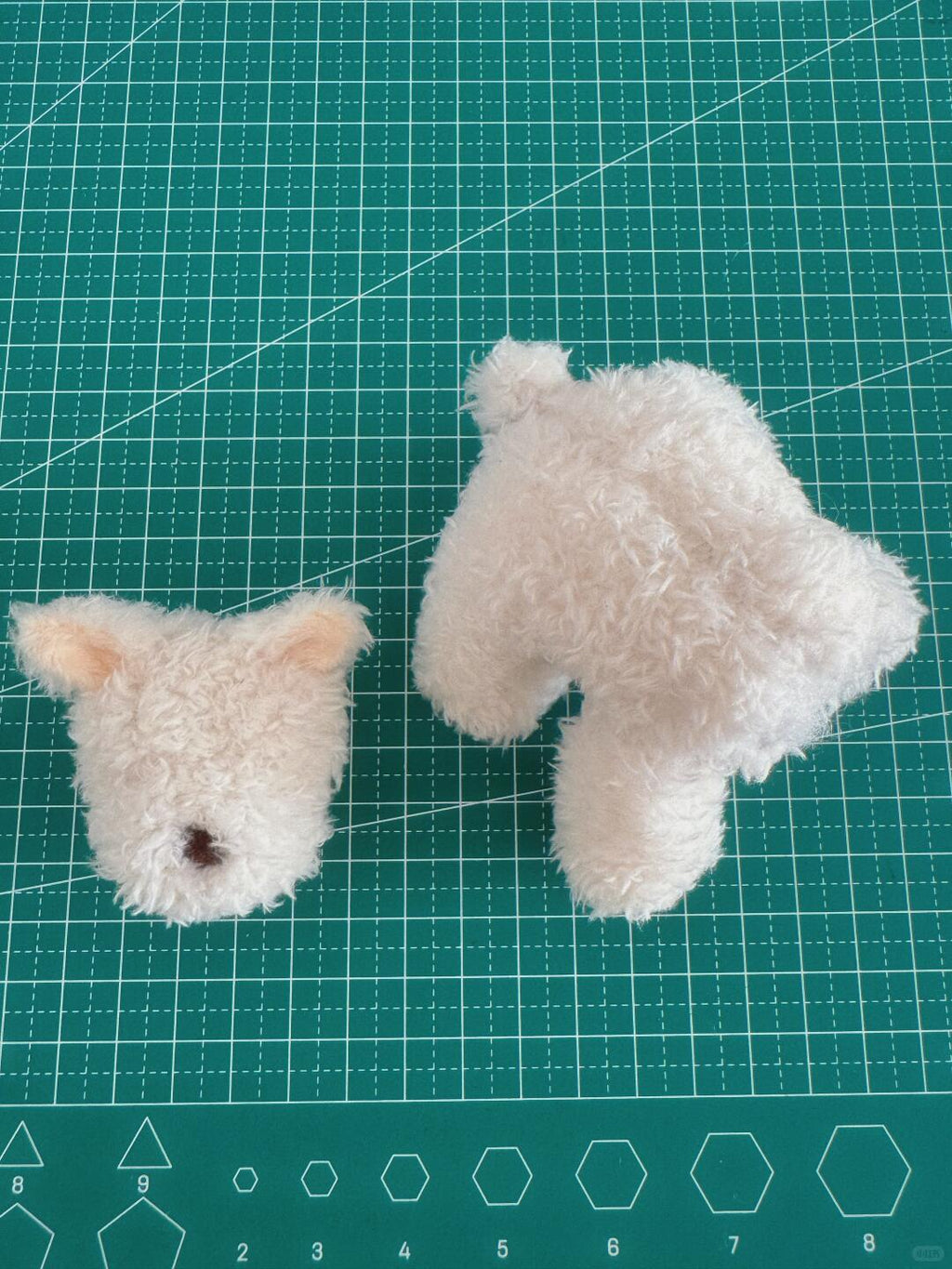 Two white plush dog toys on a green cutting mat with grid lines.