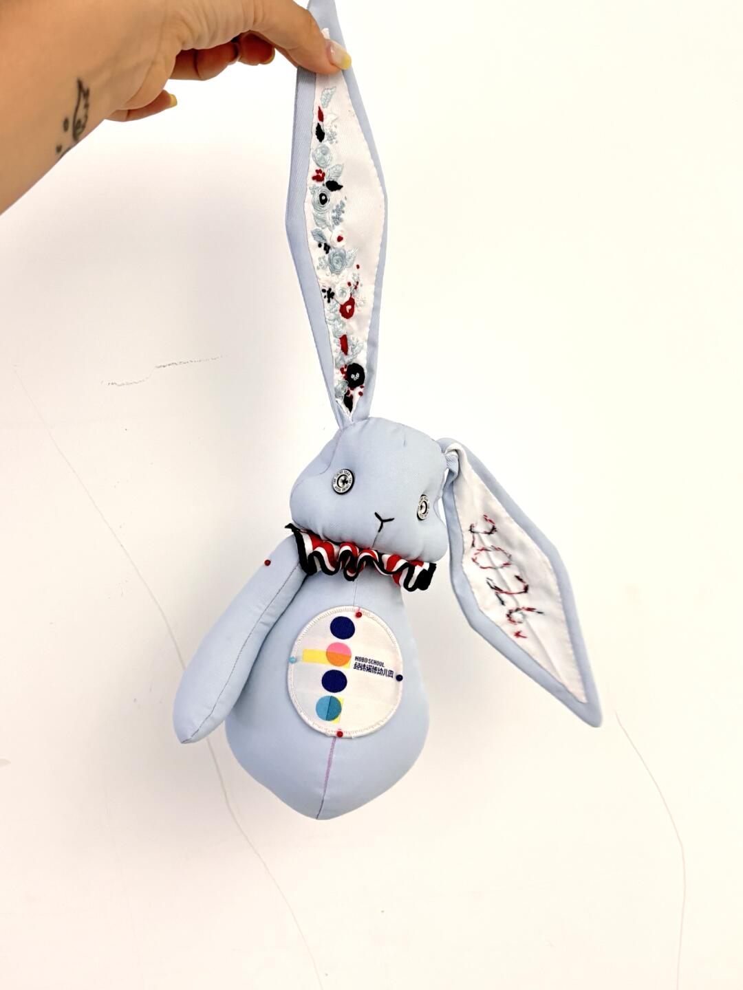 Finished light blue denim bunny plush hanging from one embroidered ear against a pale background.