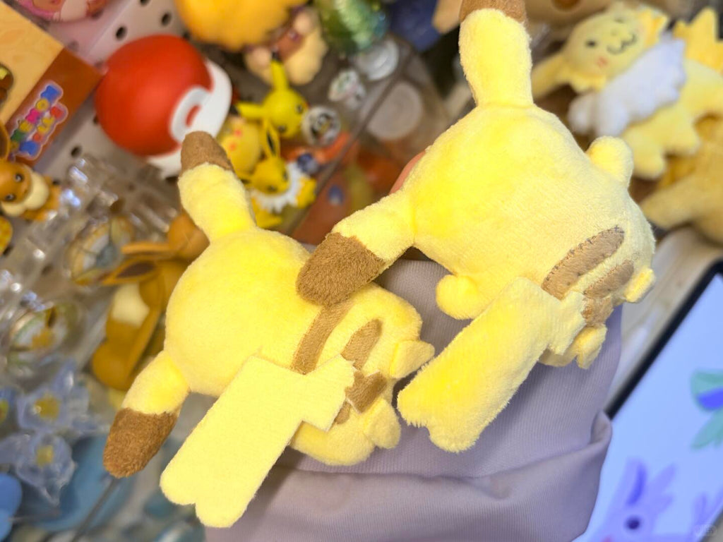 Plush toy resembling a Pikachu  with brown accents on a blurred background of other toys.