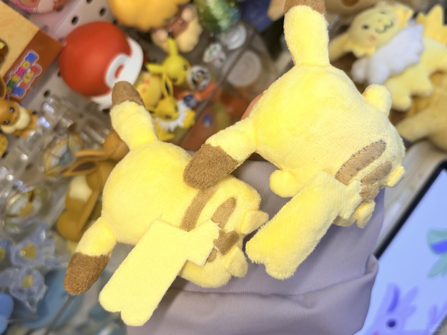 Plush toy resembling a Pikachu  with brown accents on a blurred background of other toys.