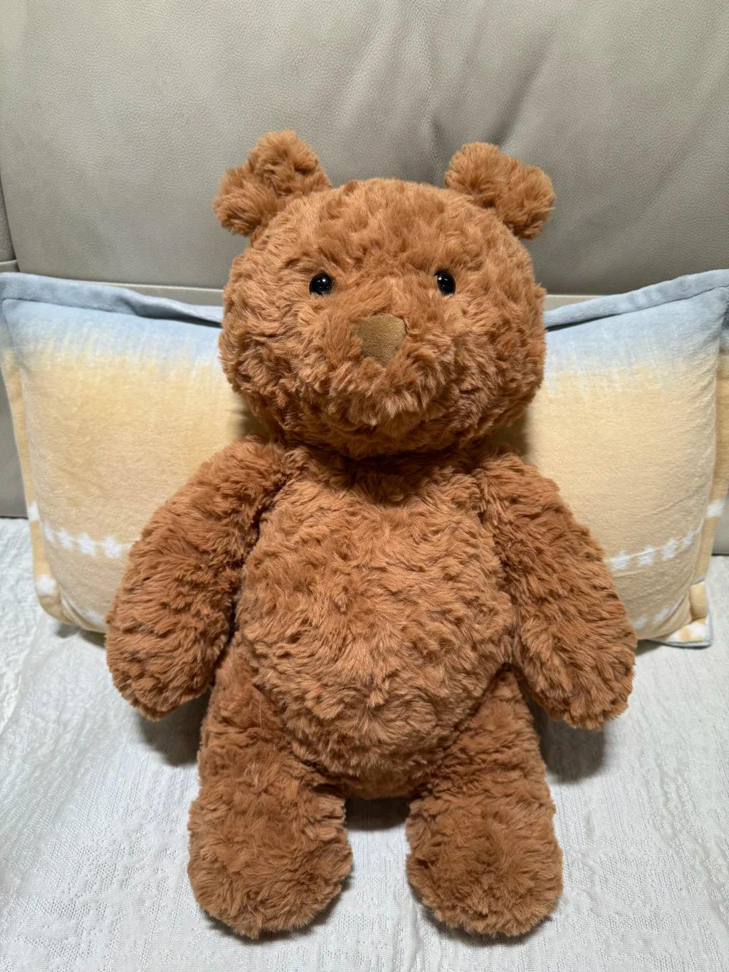 Brown teddy bear sitting on a light-colored surface with a neutral background