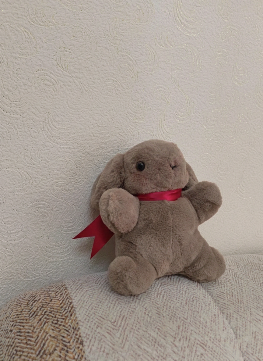 Brown plush toy with a red ribbon on a textured beige surface