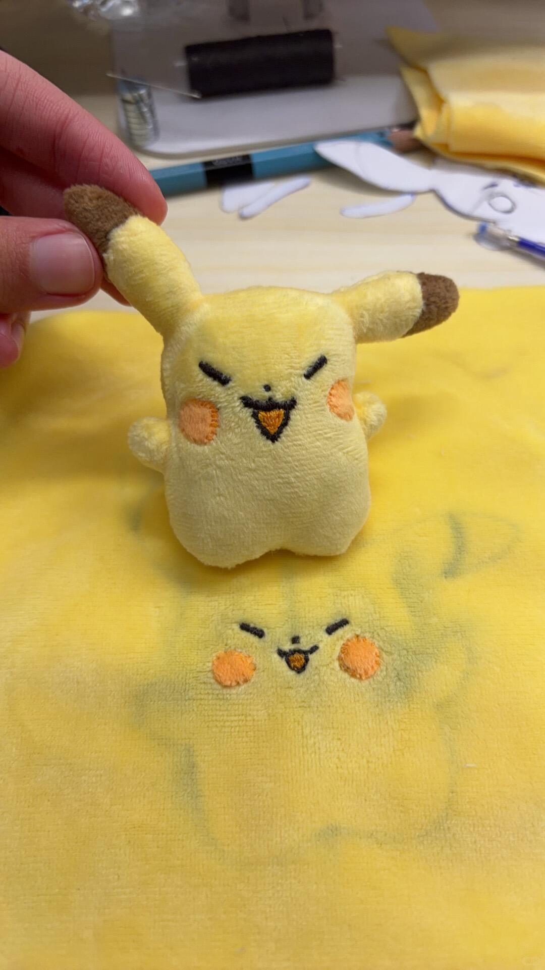 Small plush toy resembling Pikachu held over a larger yellow fabric with similar design.