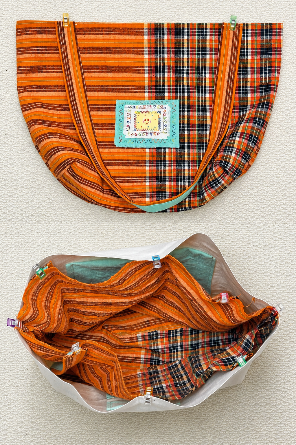 An orange and black plaid fabric bag shown from the front and inside, mounted on a textured off-white wall. The front view shows a central sewn label reading 'ORLANDO BAKERS CRAFTS', and the inside view shows a white lining and green fabric lining.