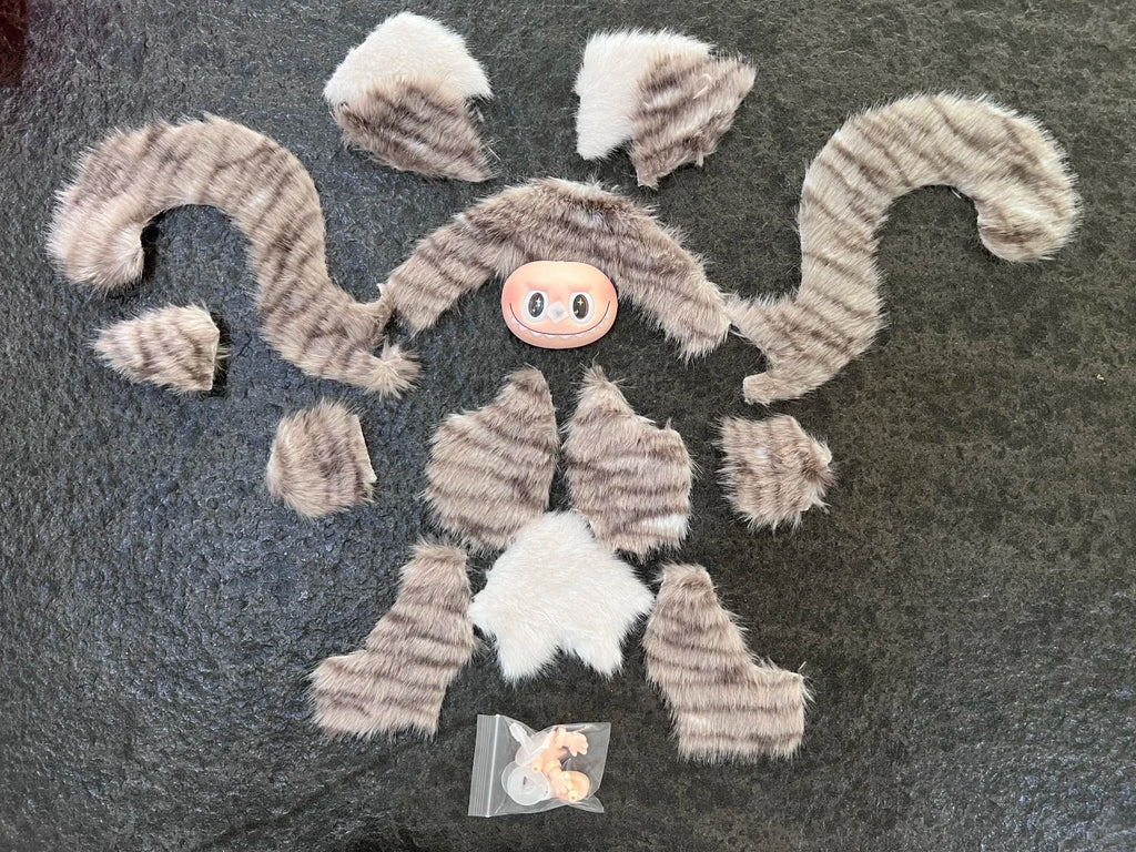 Labubu cat sewing pattern. Fur-like material pieces on a dark surface with a small pink object in the center. 