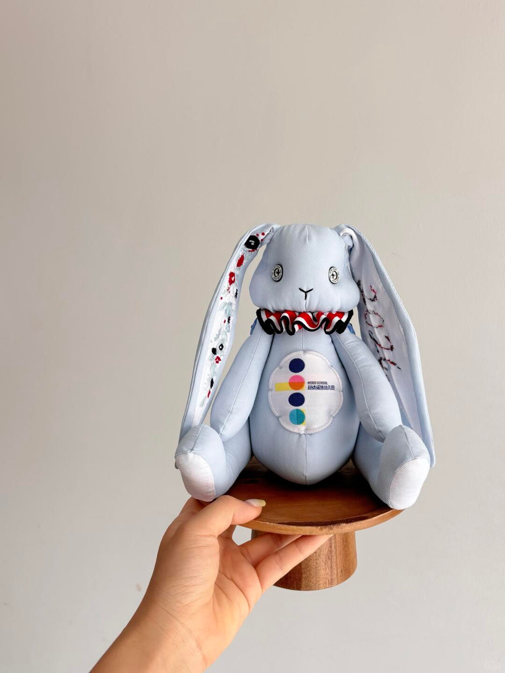 Light blue denim bunny plush seated on a small wooden stand, with embroidered ears and a ruffled collar.