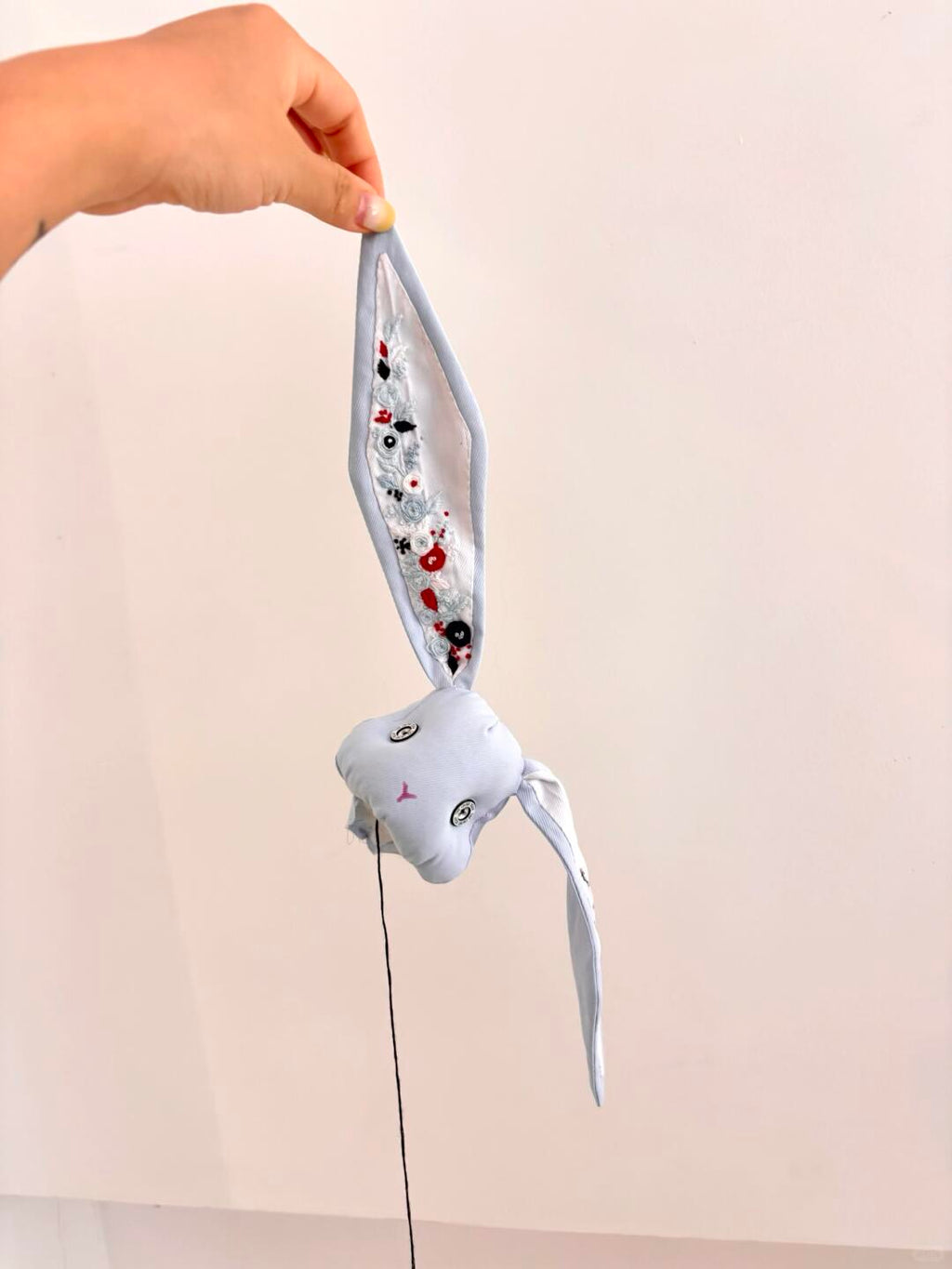 Light blue denim bunny plush suspended by one embroidered ear, showing its long limbs and stitched face.