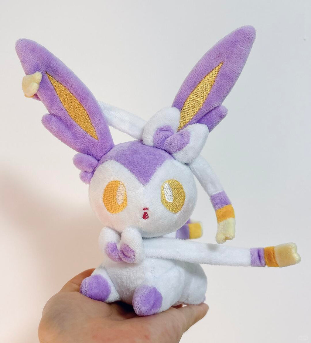 Plush toy of a Sylveon  character with purple and white colors held by a hand against a light background