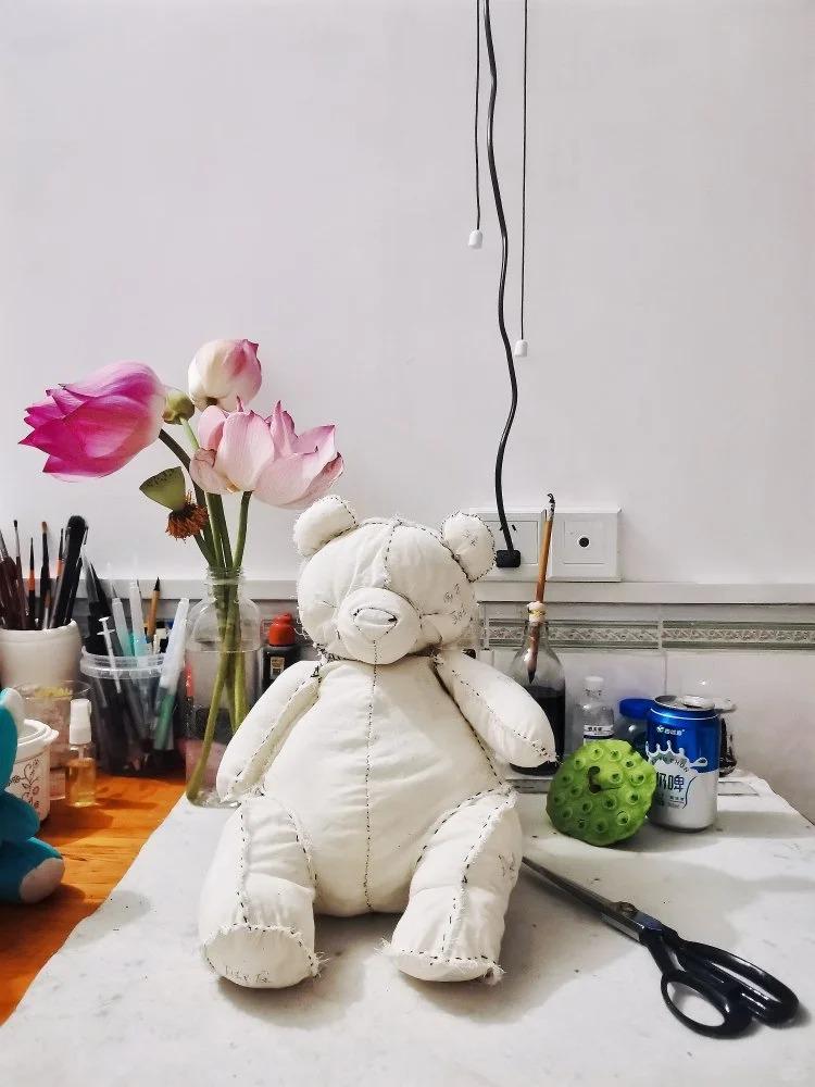White teddy bear on a table with flowers and various items in the background