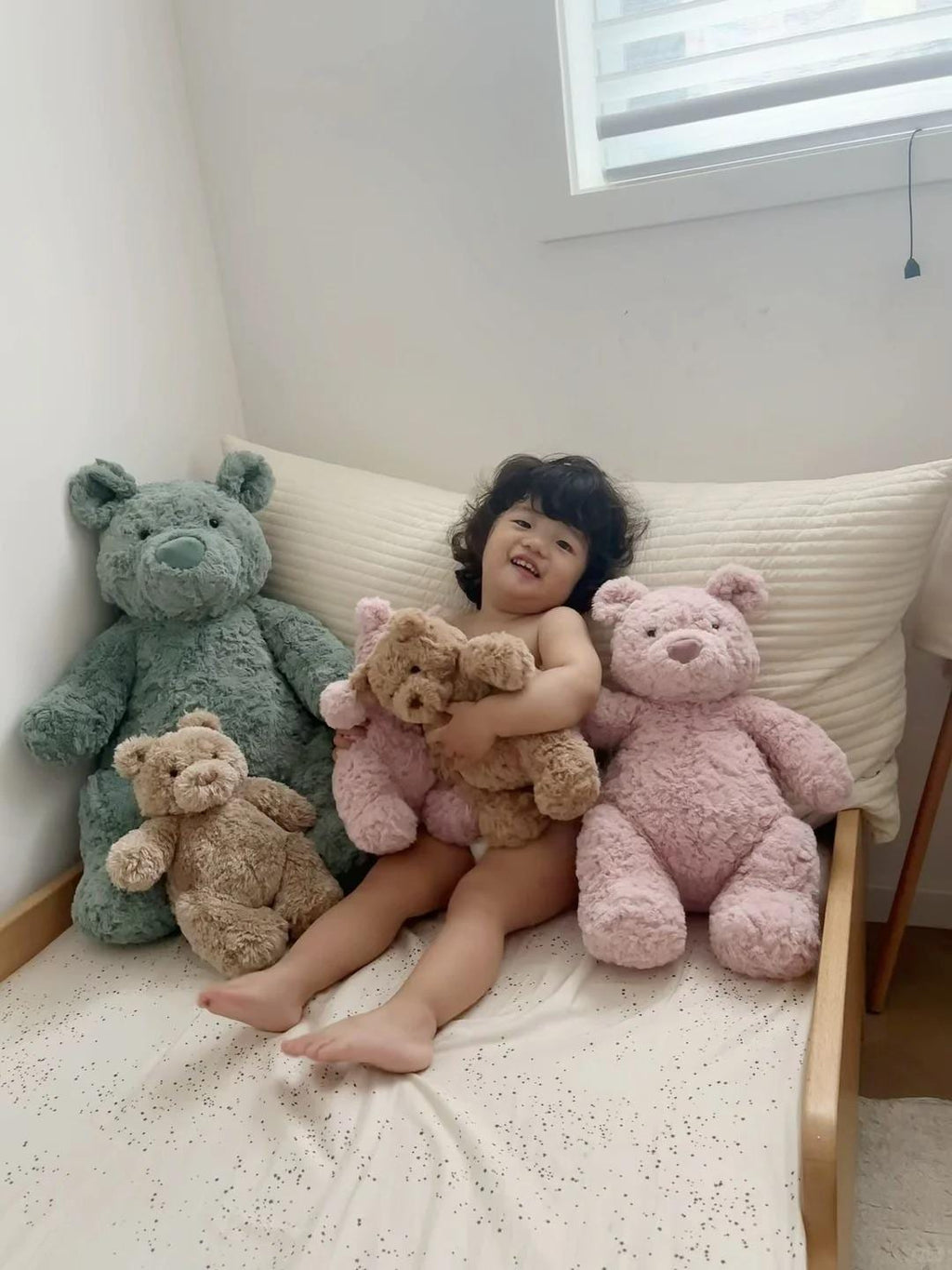 Child sitting on a bed with teddy bears in a cozy room.