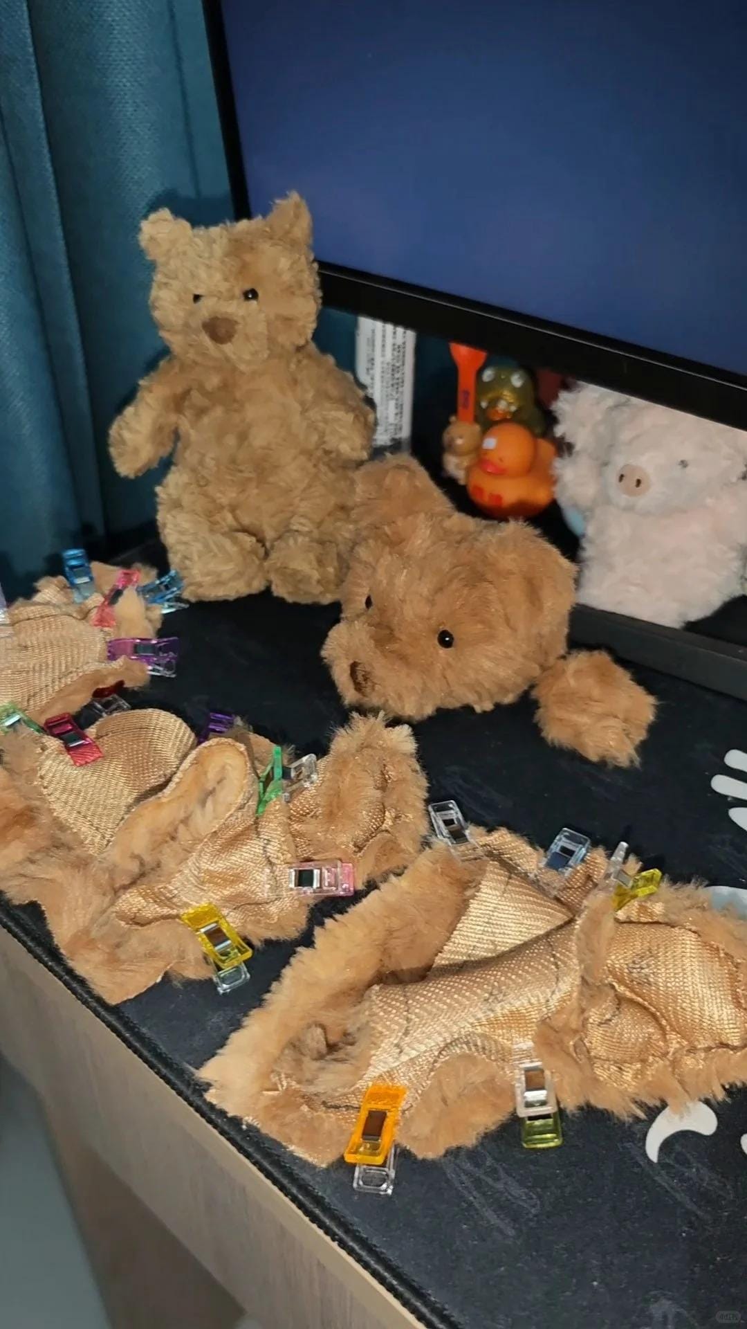 Collection of teddy bears with clothespins on a surface, with a television screen in the background.