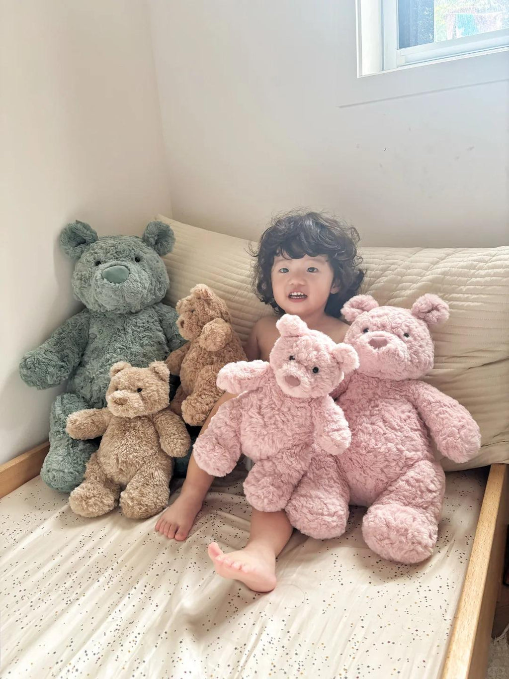 Child sitting on a bed with teddy bears of different colors