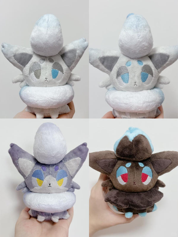 Four views of plush toy Zorua plushies resembling a cute icy creature, shown held in hands against a plain light background. The top two are light gray and white with blue accents, and the bottom two are lavender-gray and dark brown with blue, red, and yellow accents.