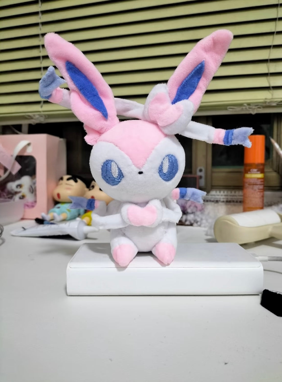 Plush toy Sylveon  resembling a character with pink and blue accents on a desk.
