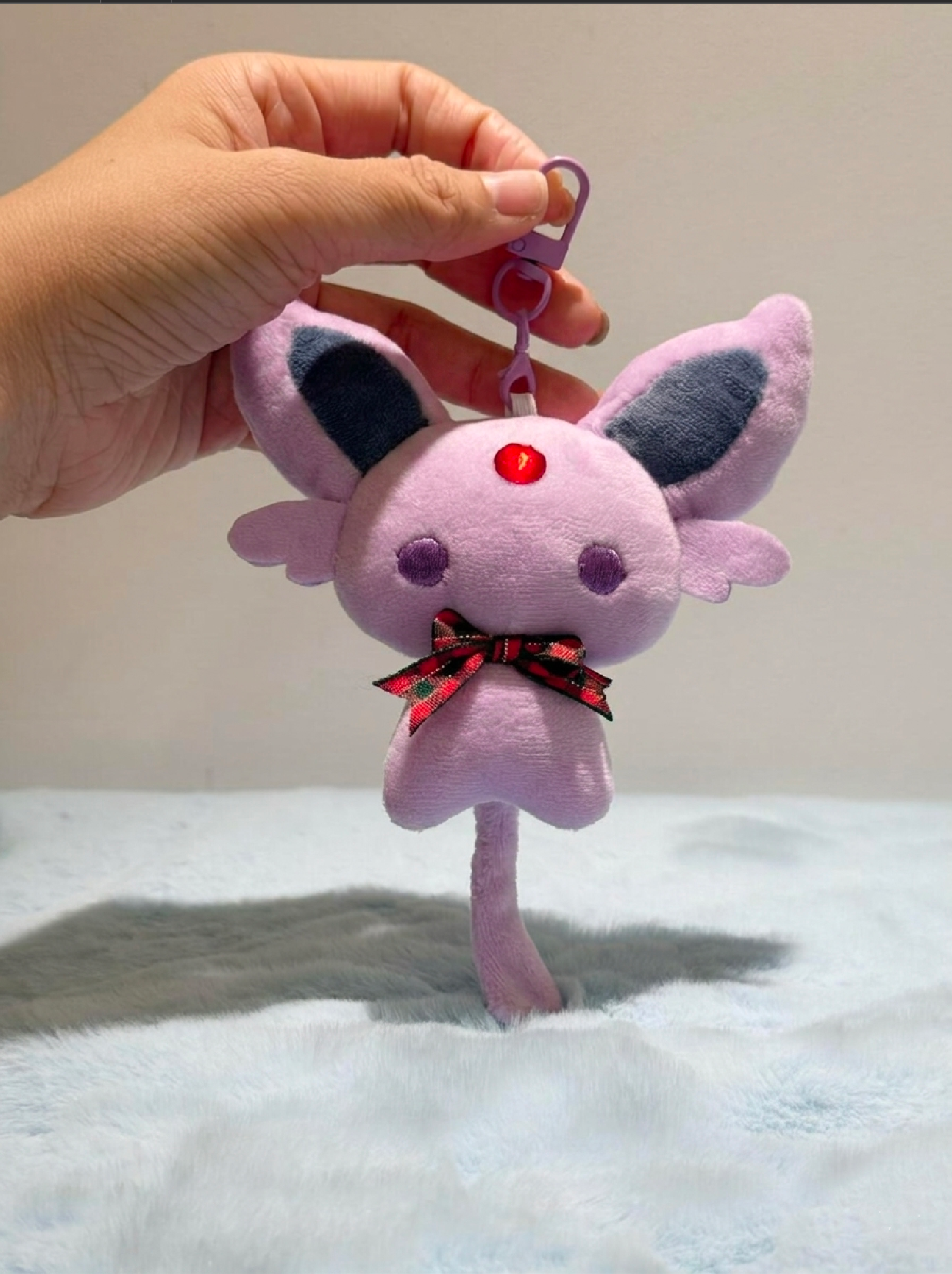 Purple Espeon plush keychain with a red button and black bow held by a hand on a light background