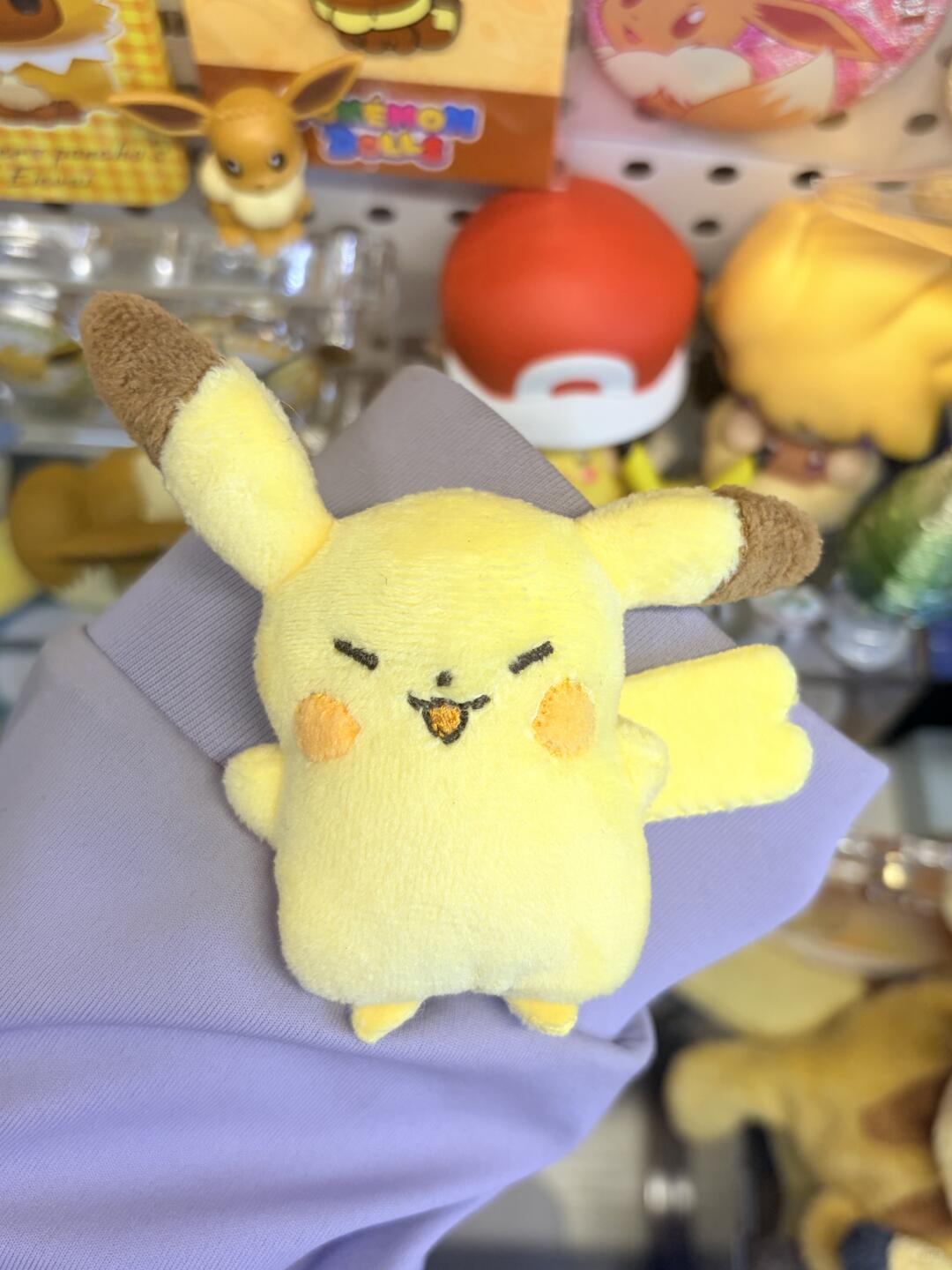Plush toy resembling Pikachu held by a gloved hand with a store display in the background.