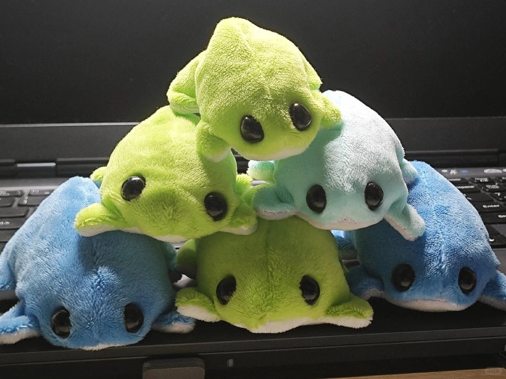 Six blue and green frog plush toys with white bellies stacked in a pyramid on a laptop.