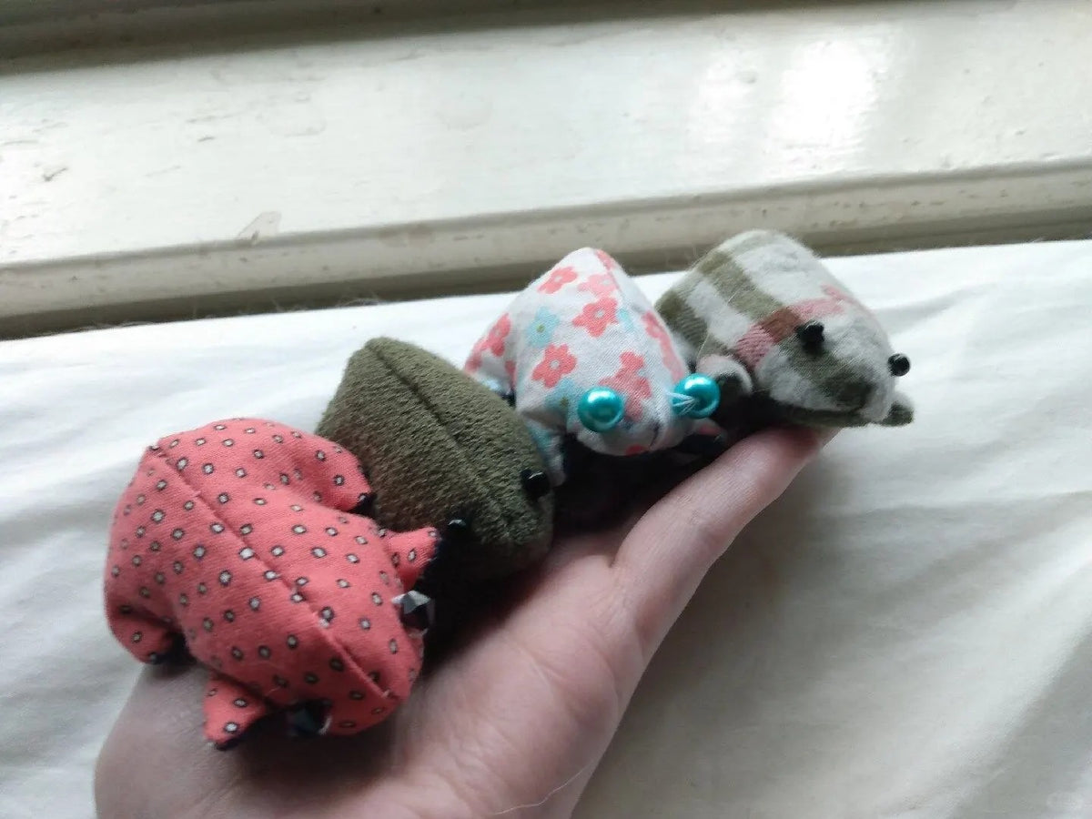Four miniature fabric frogs in solid and floral prints balanced across a hand.