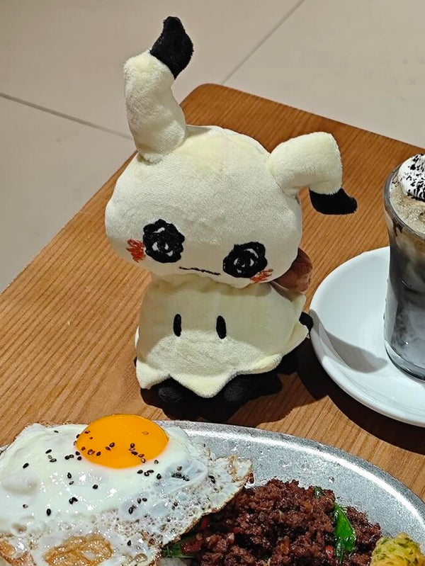 Mimikyu plush displayed beside a plate of food in a cafe