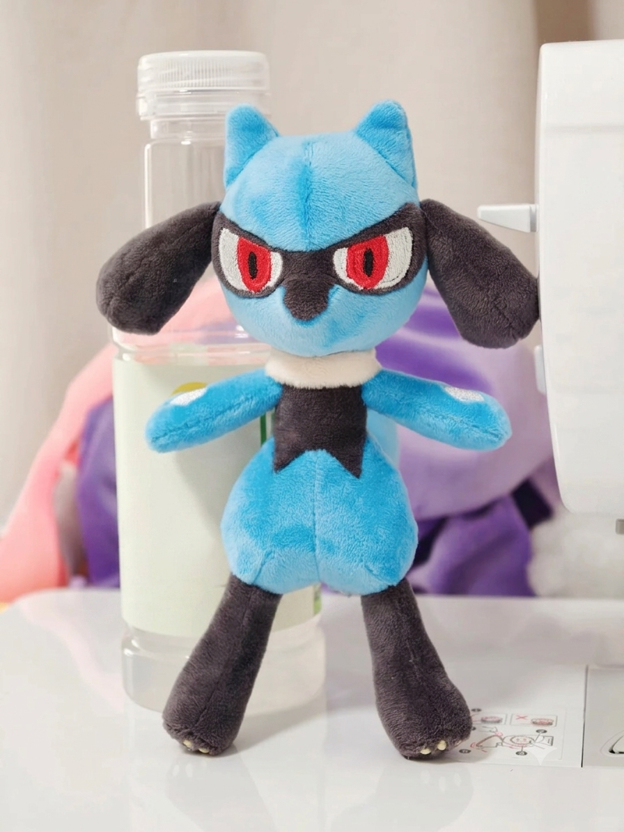 Front view of a handmade Lucario-inspired plush showing embroidered red eyes, blue body and black facial details